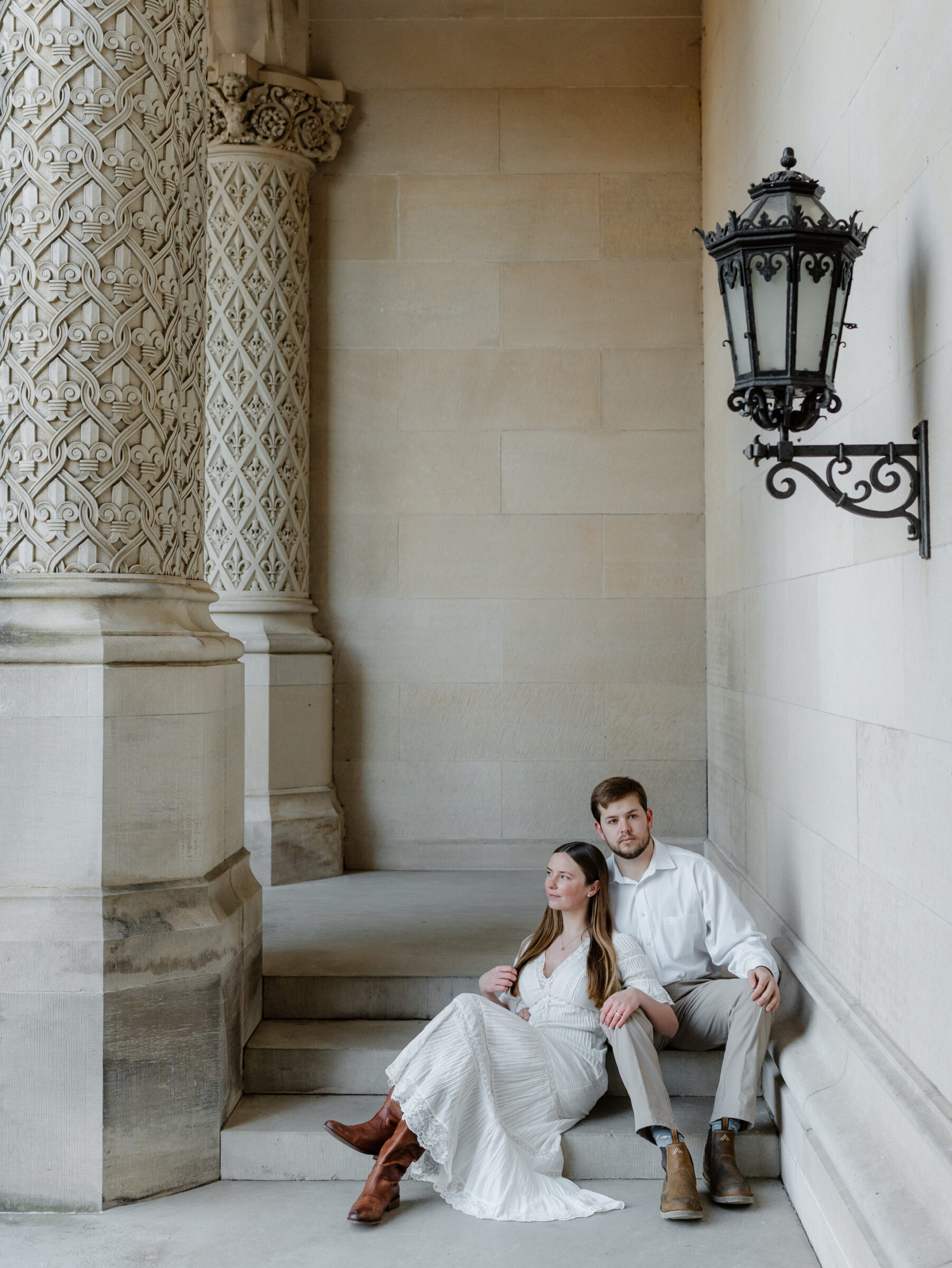 Couple seated on stone steps beneath the arches at the Biltmore Estate during an editorial engagement session in Asheville NC