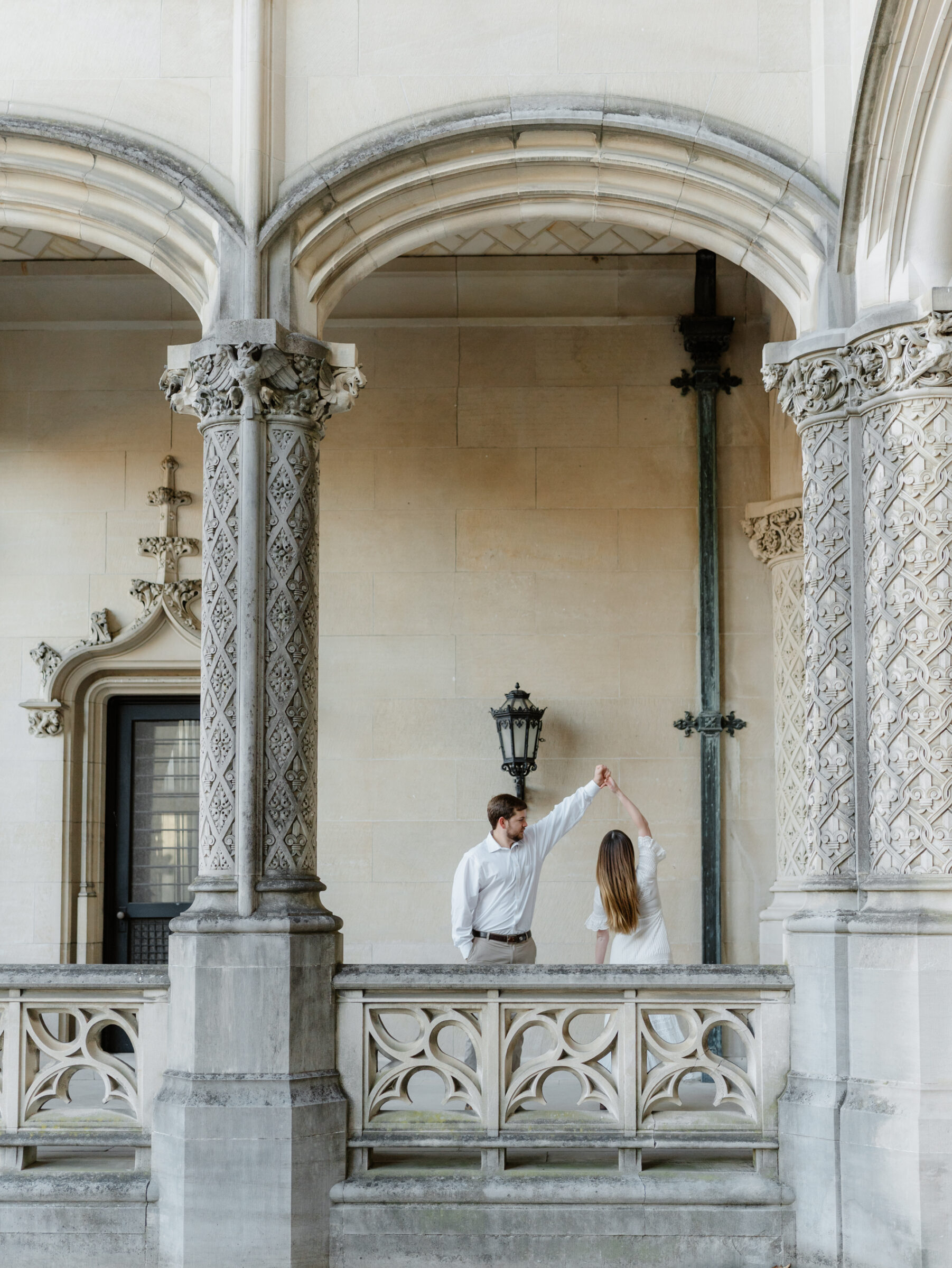 Wide editorial portrait of a couple sharing a quiet moment beneath ornate stone arches
