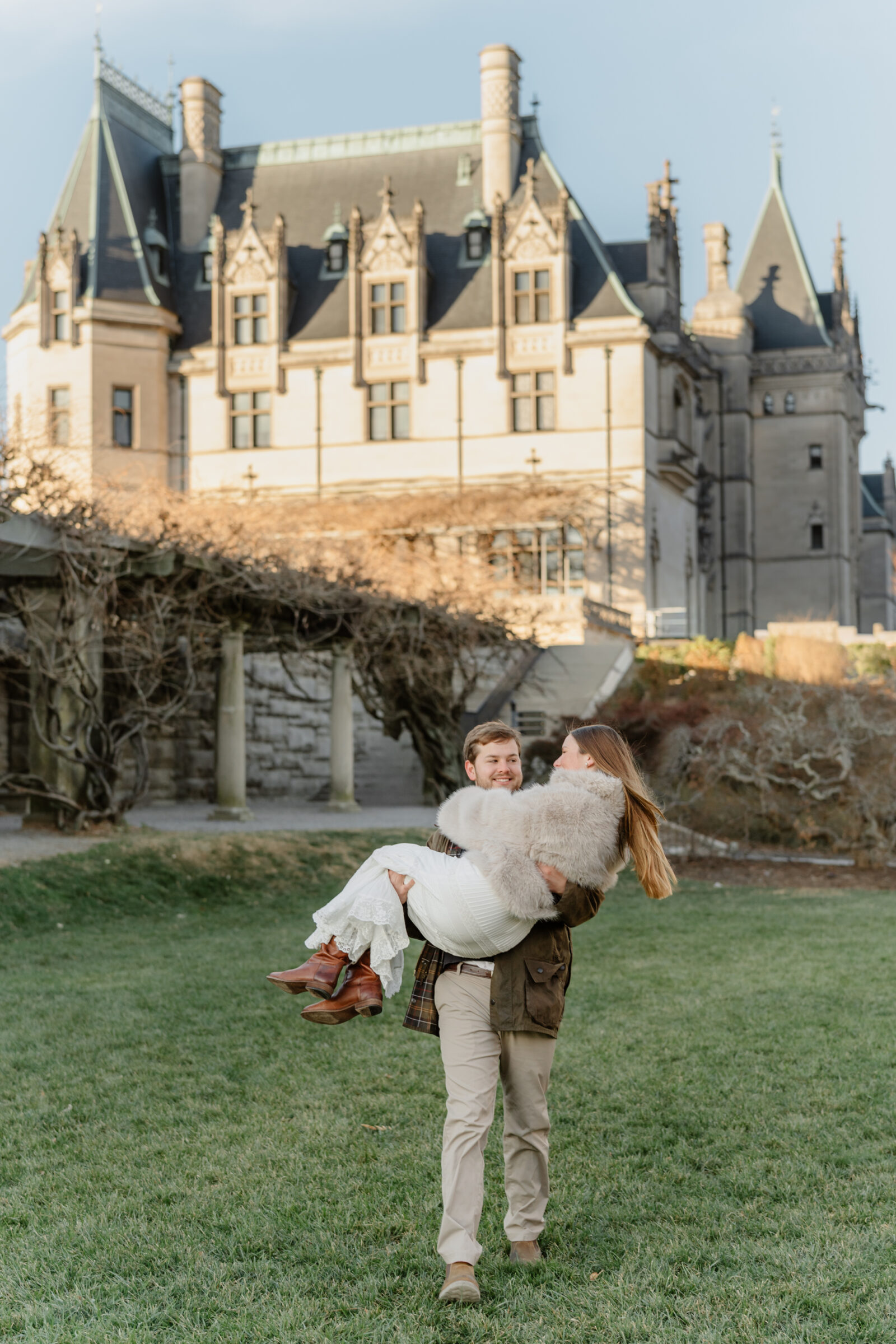 Playful engagement portrait of a couple laughing together on the lawn in front of the Biltmore Estate at sunset