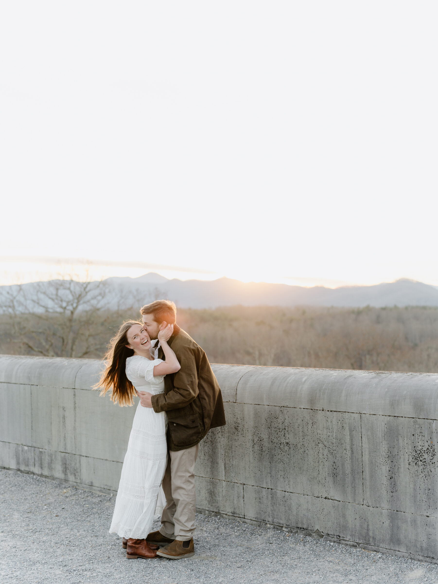 Asheville NC Engagement Photographer | Romantic wide portrait of a couple embracing together at sunset with mountain views in the distance