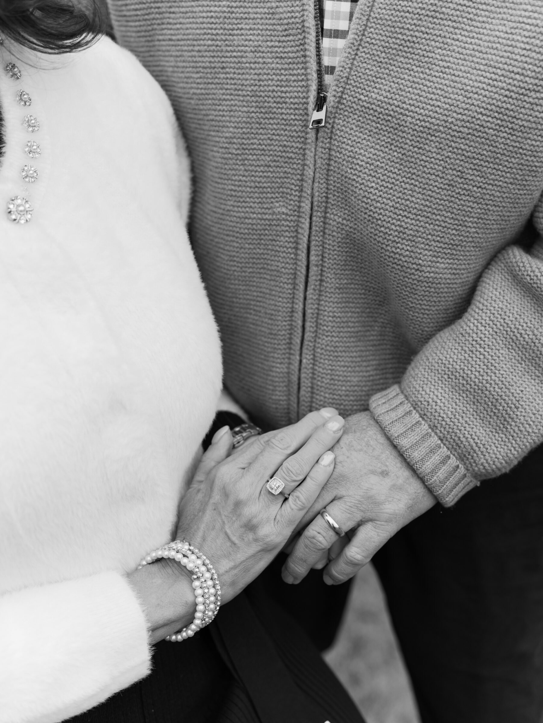Close-up of parents holding hands during a late fall family photo session, highlighting winter layers and details
