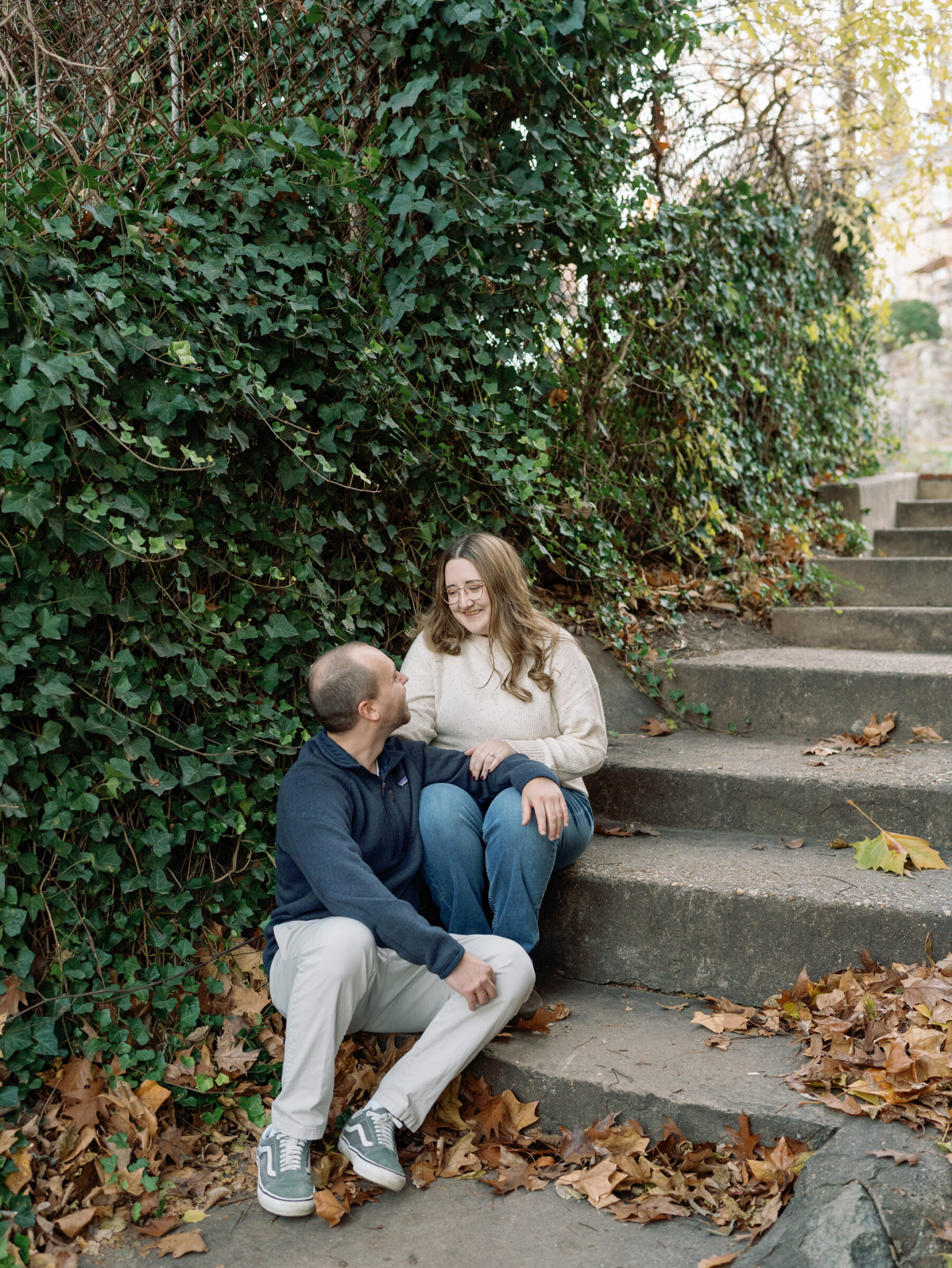 Couple sitting together on stone steps surrounded by ivy and fallen autumn leaves during their Occoquan engagement session.
