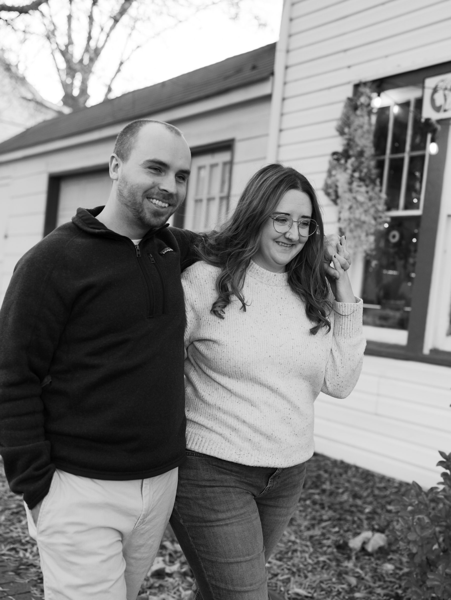 Couple walking closely together in Historic Occoquan, smiling as they pass a storefront during their fall engagement session.