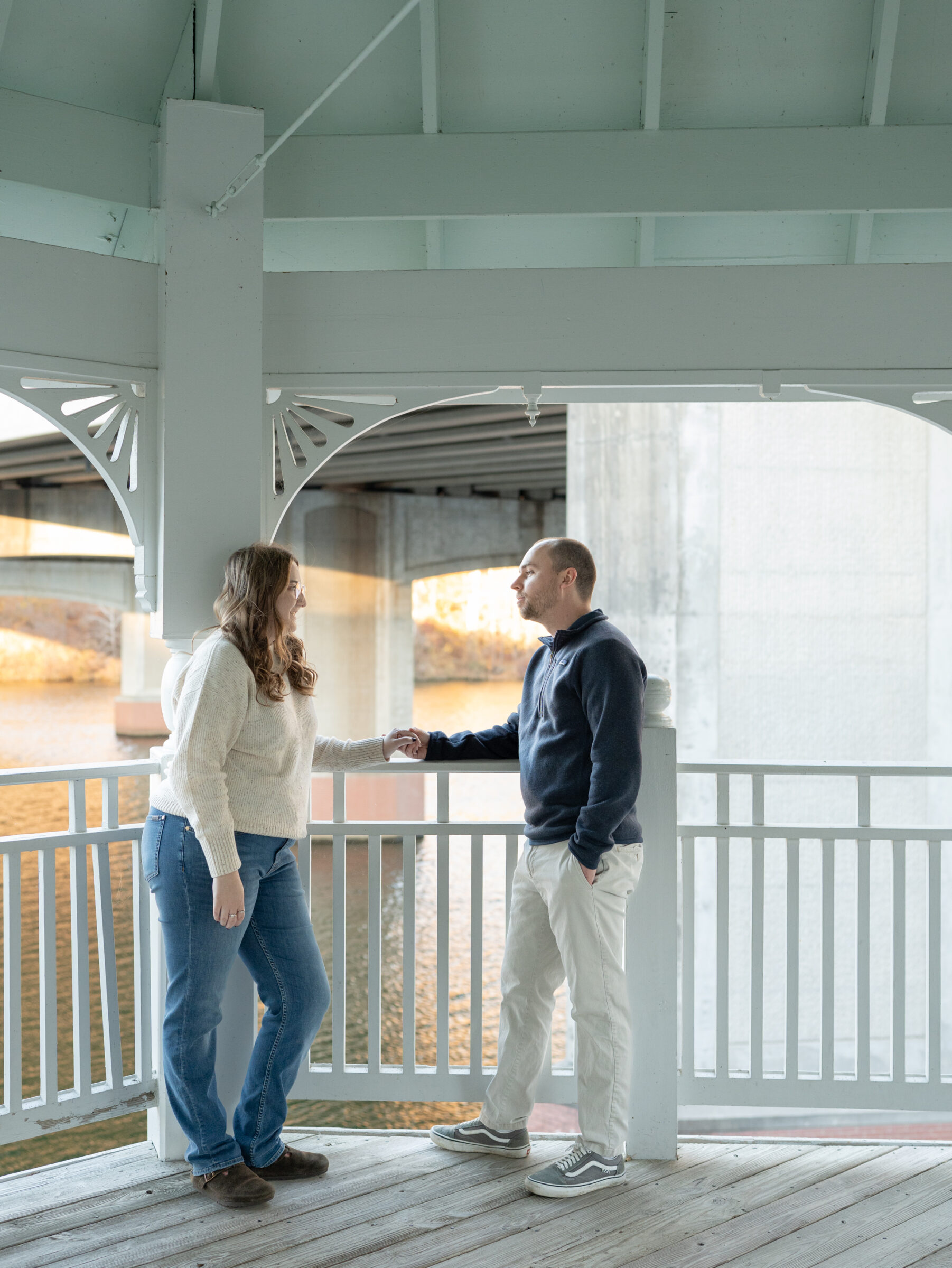 Couple holding hands and talking inside a waterfront gazebo during their fall engagement session.