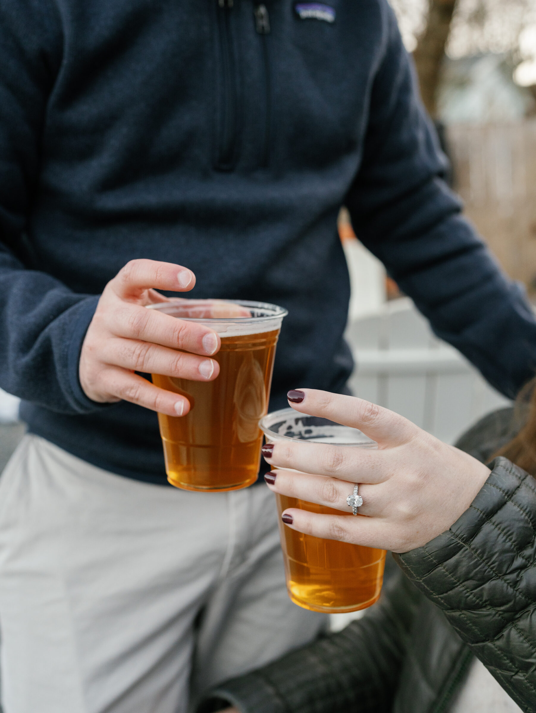 Close-up of the couple clinking plastic cups of beer, with the engagement ring visible on her hand.