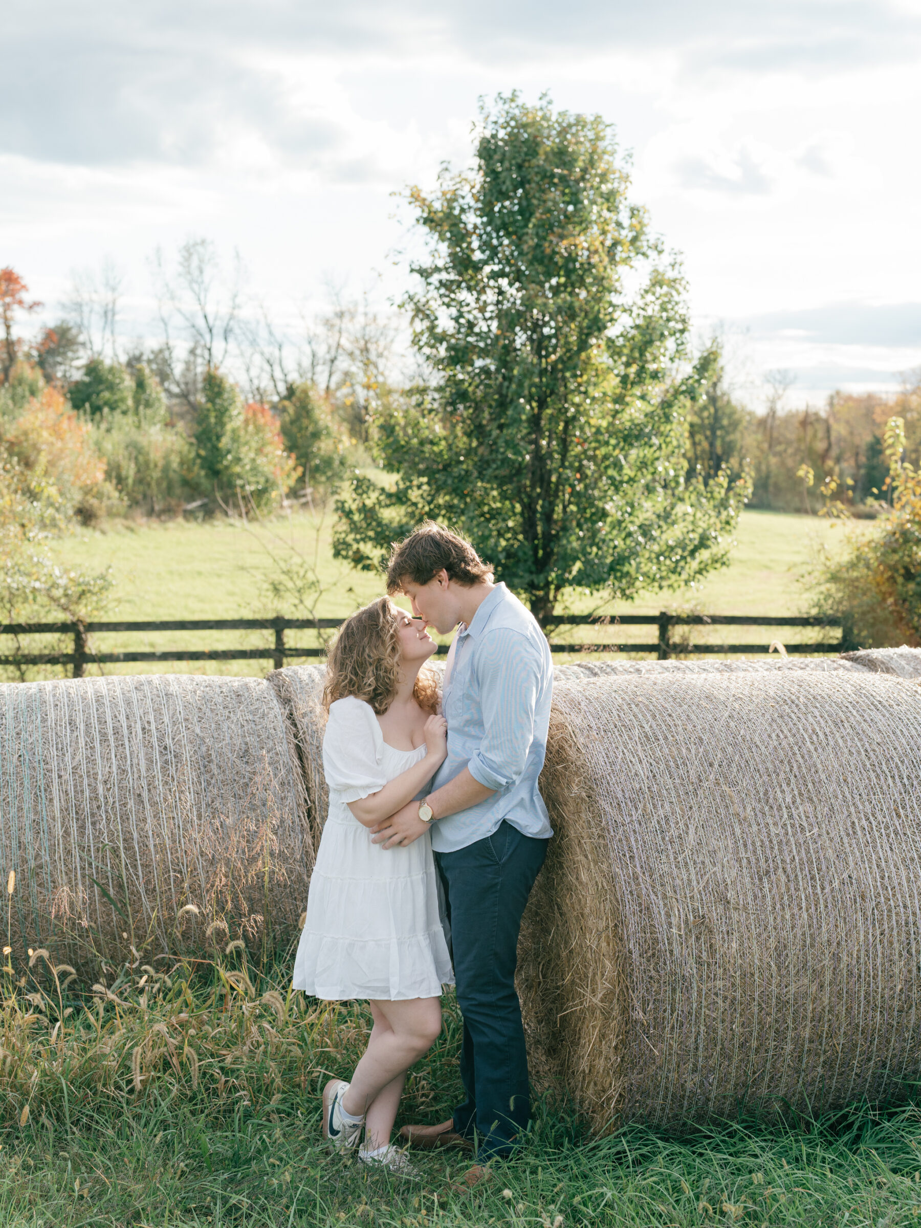 Engaged couple sharing a quiet moment beside hay bales on their Lovettsville, Virginia property at sunset