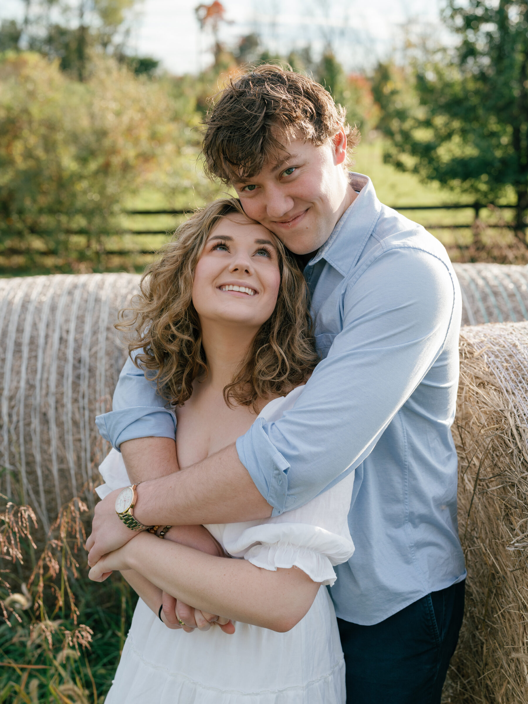 Engaged couple embracing beside hay bales during a relaxed at-home engagement session in Lovettsville, Virginia