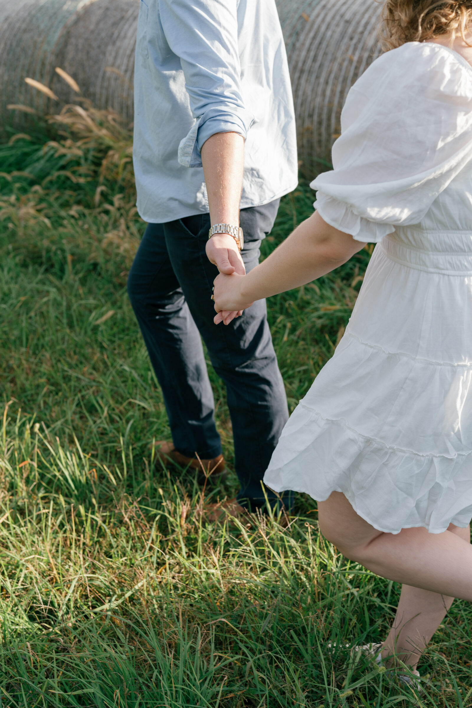 Engaged couple walking hand in hand through a grassy field during an at-home engagement session in Lovettsville, Virginia