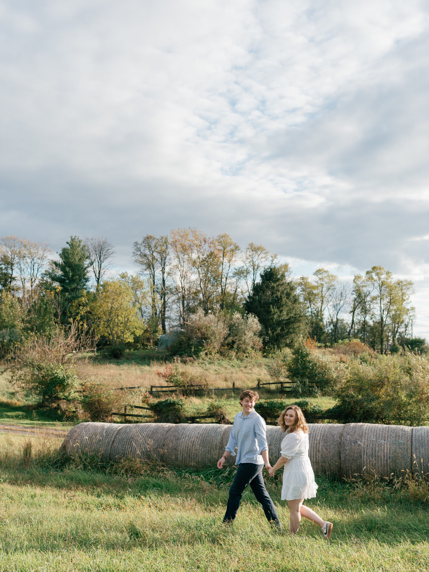 Wide landscape view of an engaged couple walking together across their Lovettsville, Virginia property during an at-home engagement session