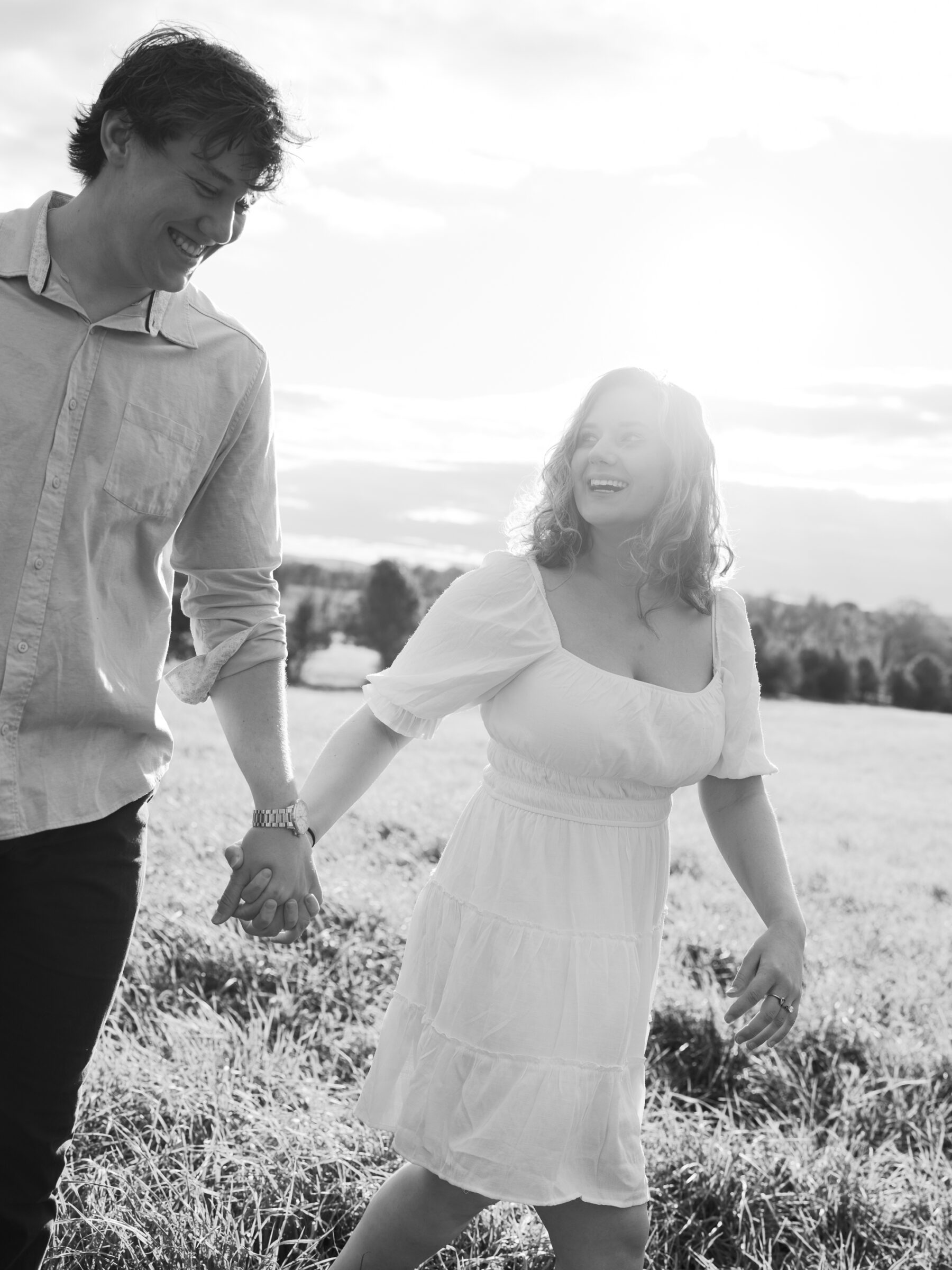 Lovettsville VA Wedding Photographer | Black and white engagement photo of a couple walking hand in hand across a field during an at-home session in Lovettsville, Virginia