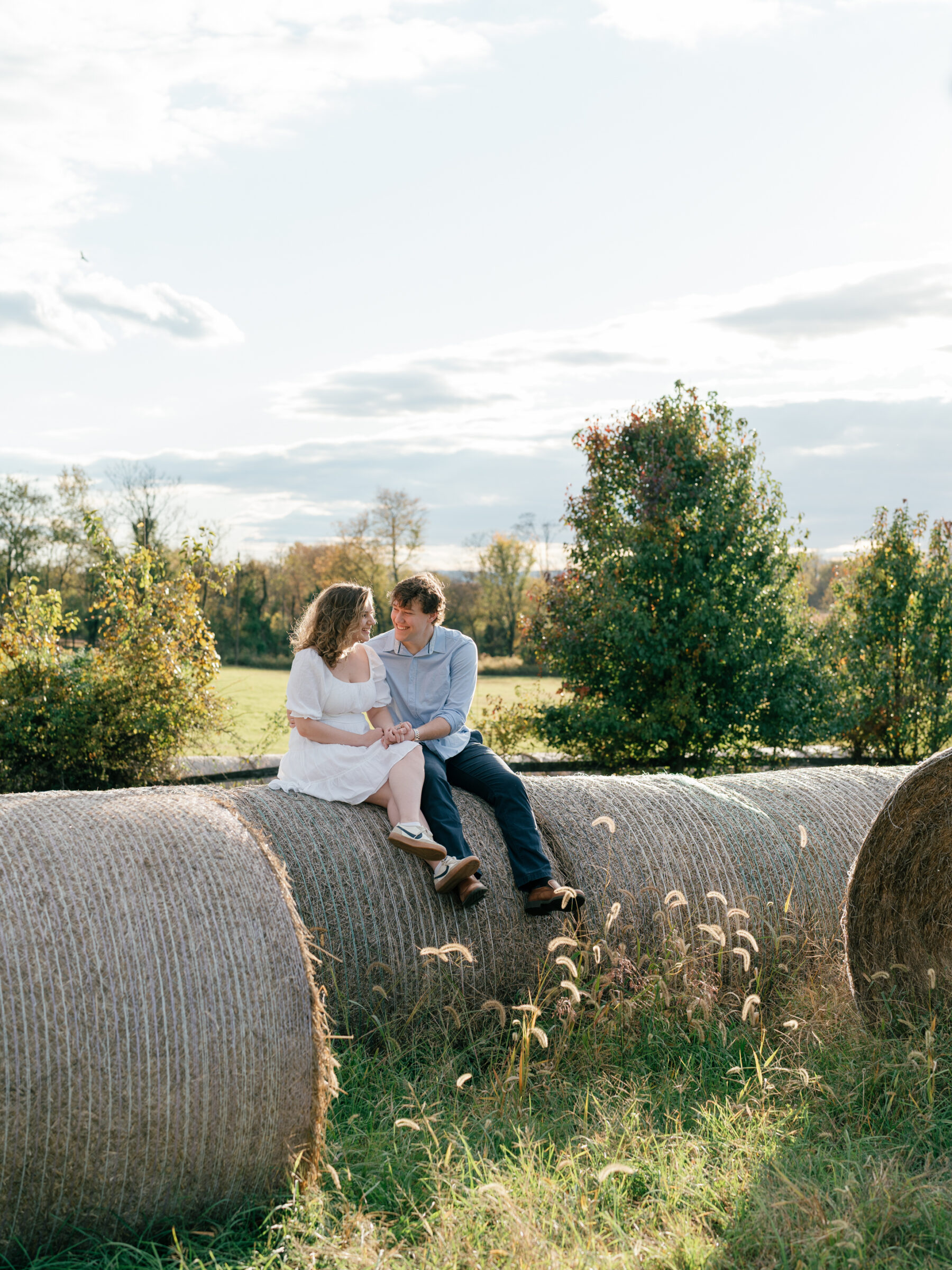 Lovettsville VA Wedding Photographer | Engaged couple sitting together on hay bales during a relaxed at-home engagement session in Lovettsville, Virginia