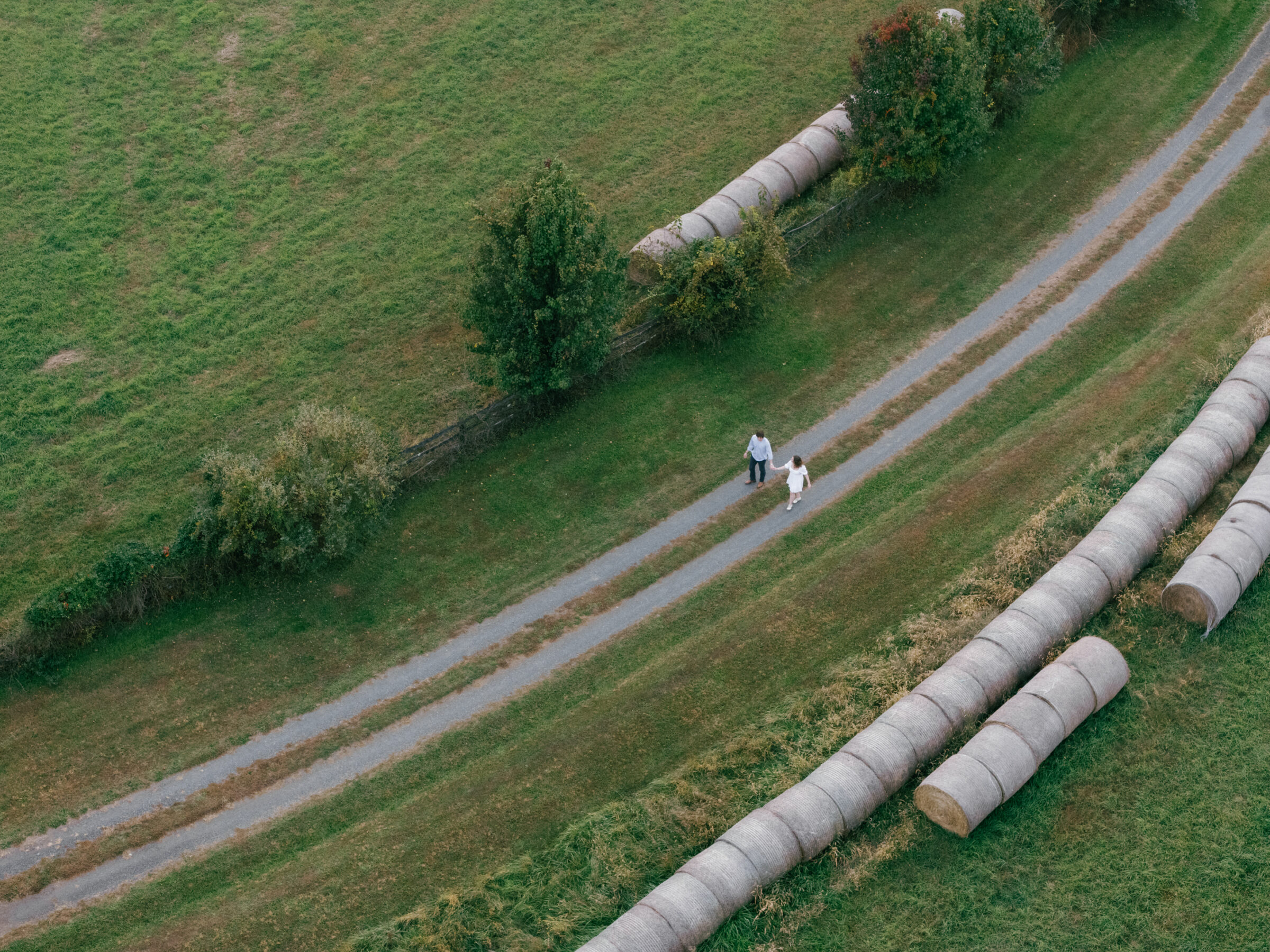 Aerial view of an engaged couple walking hand in hand along a gravel path on their Lovettsville, Virginia property during an at-home engagement session
