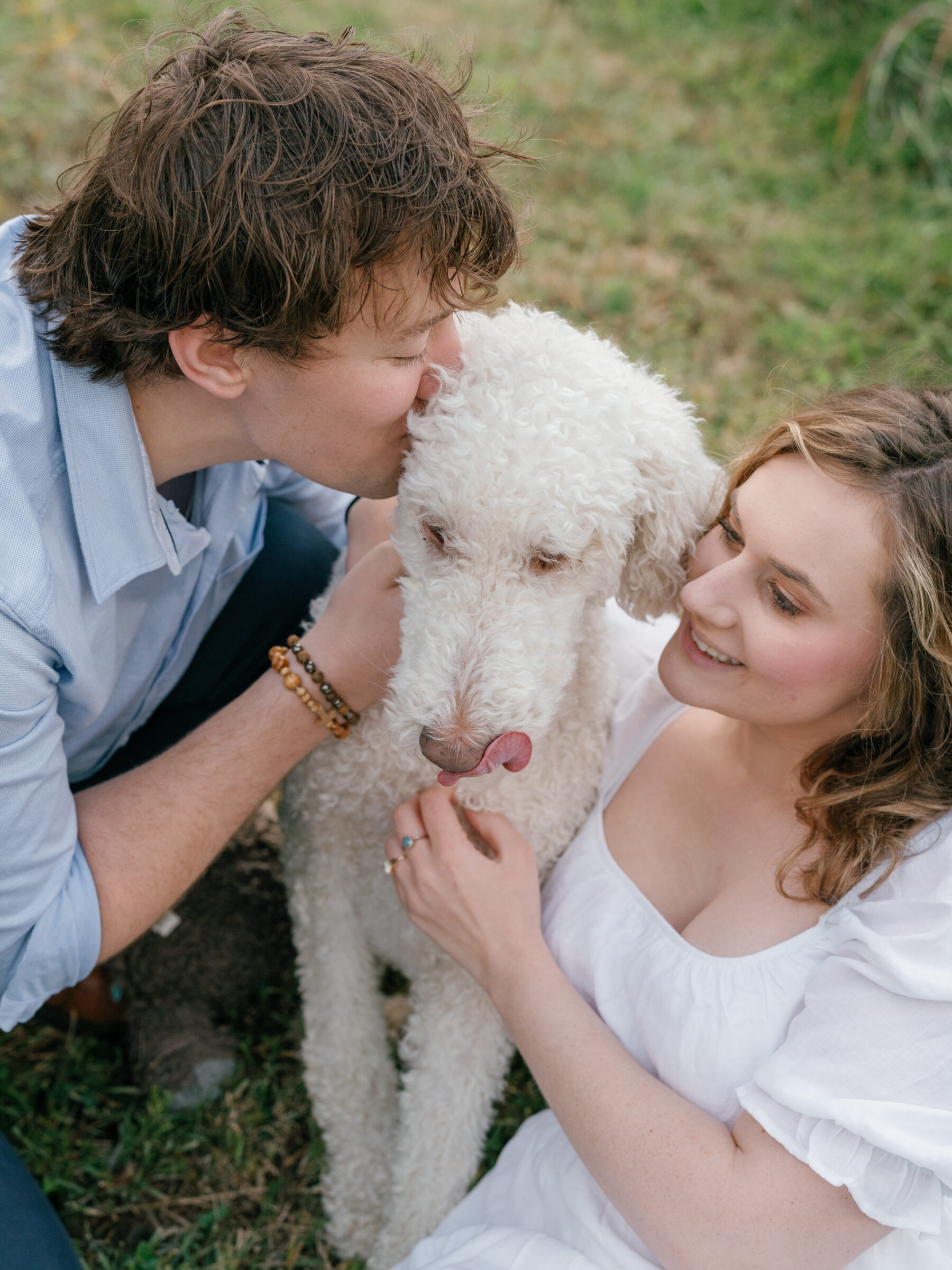 Engaged couple cuddling and kissing their dog during a playful at-home engagement session in Lovettsville, Virginia