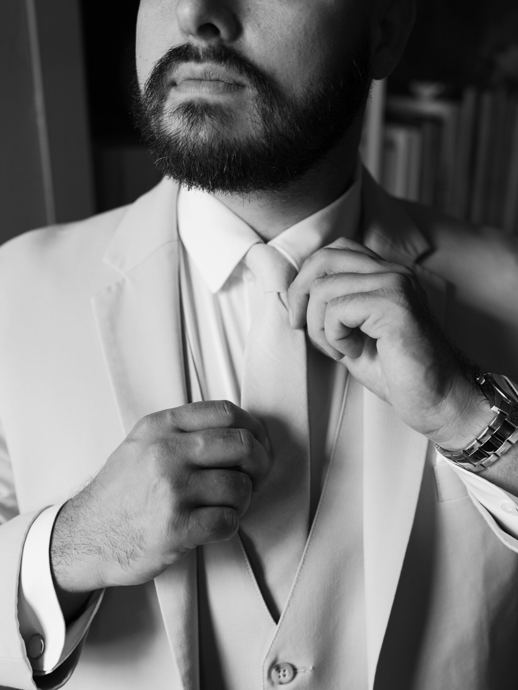 Black and white photo of the groom adjusting his tie during getting-ready moments inside Rust Manor House.
