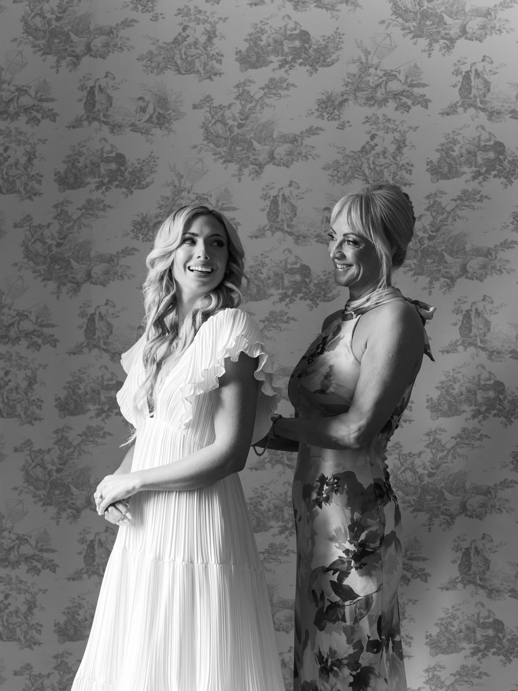 Black and white portrait of the bride smiling as a family member helps with her dress in the Rust Manor House bridal suite.