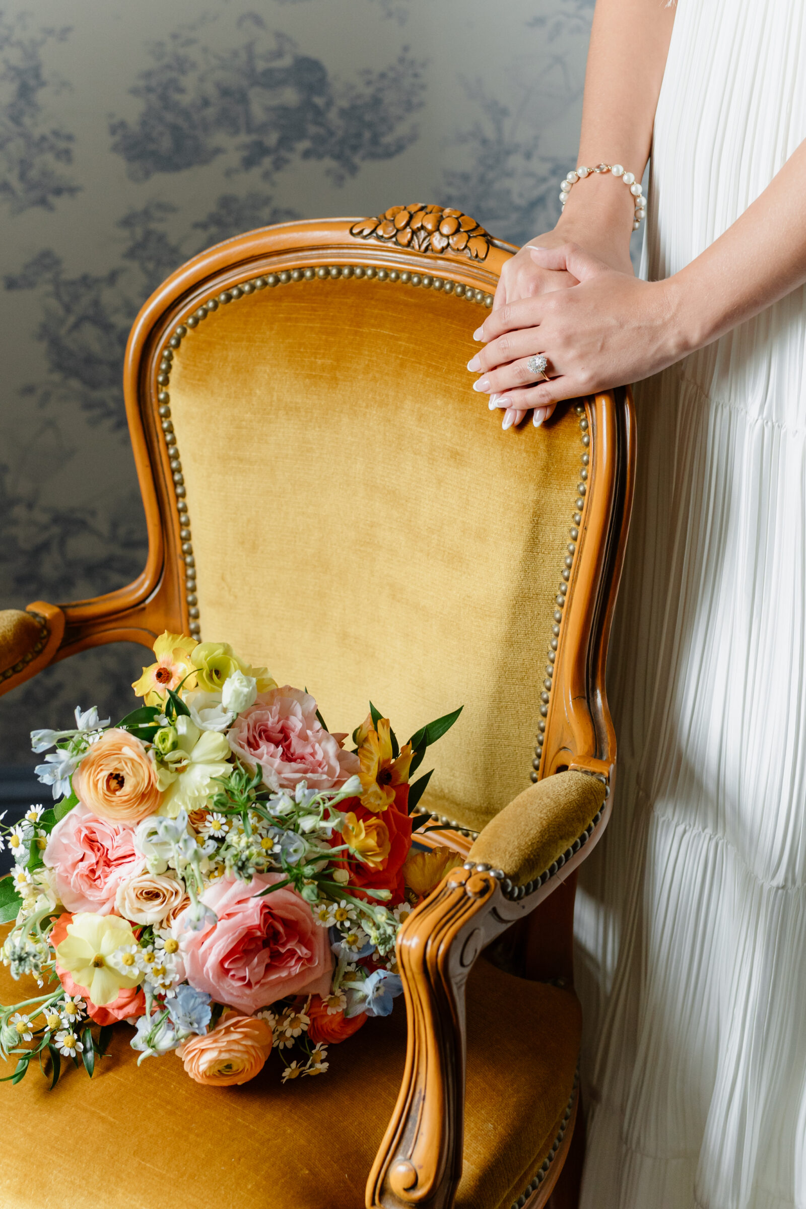 Bridal bouquet resting on a vintage gold chair as the bride’s hands rest on the back of the chair inside Rust Manor House.