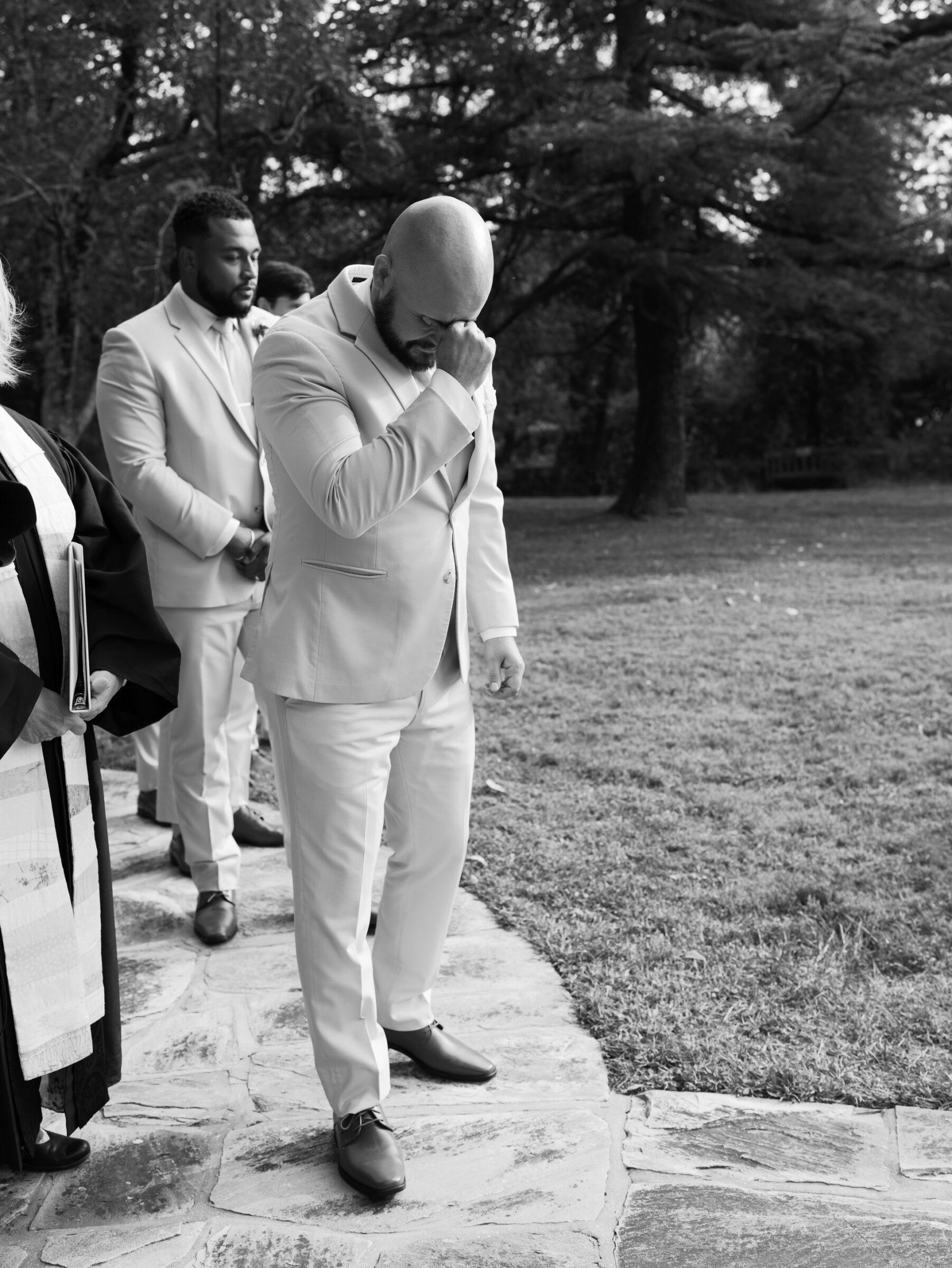 Black and white photo of the groom wiping away a tear as he walks into the garden ceremony at Rust Manor House.