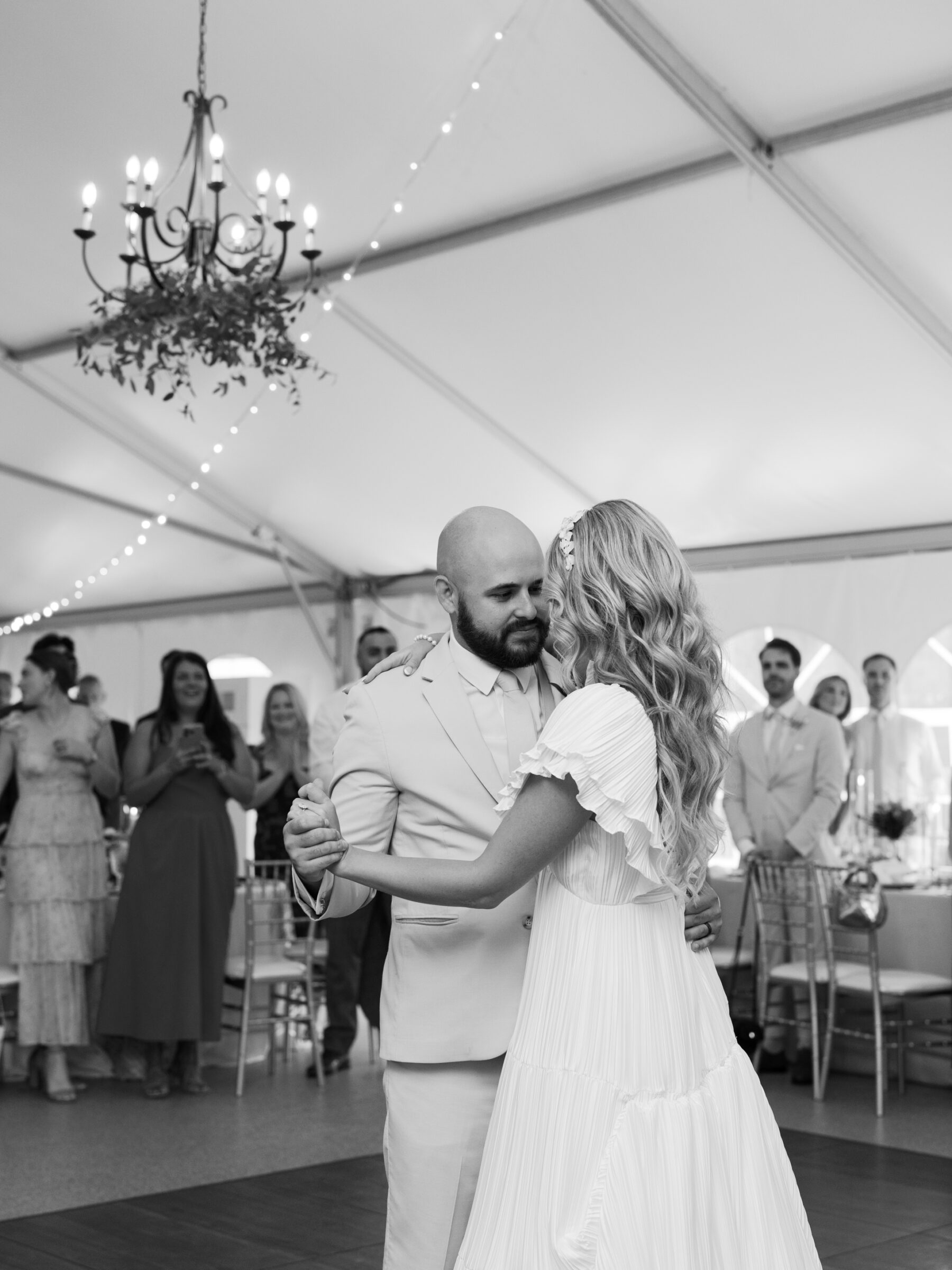 The couple dancing together during their first dance, surrounded by guests in the reception tent.