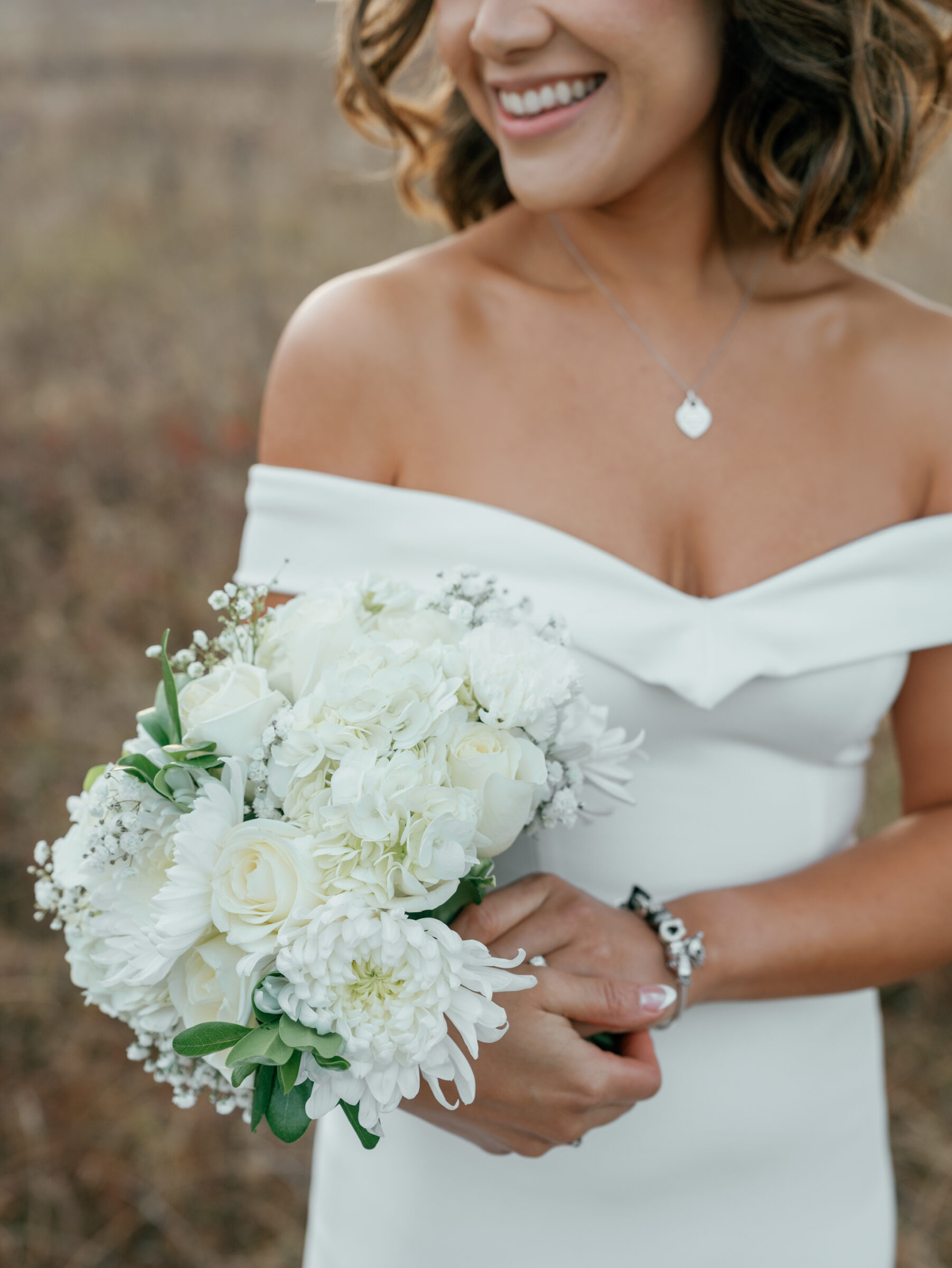 Close-up of the bride holding a white bouquet of roses and chrysanthemums, smiling softly in an autumn meadow at Tanner’s Ridge.