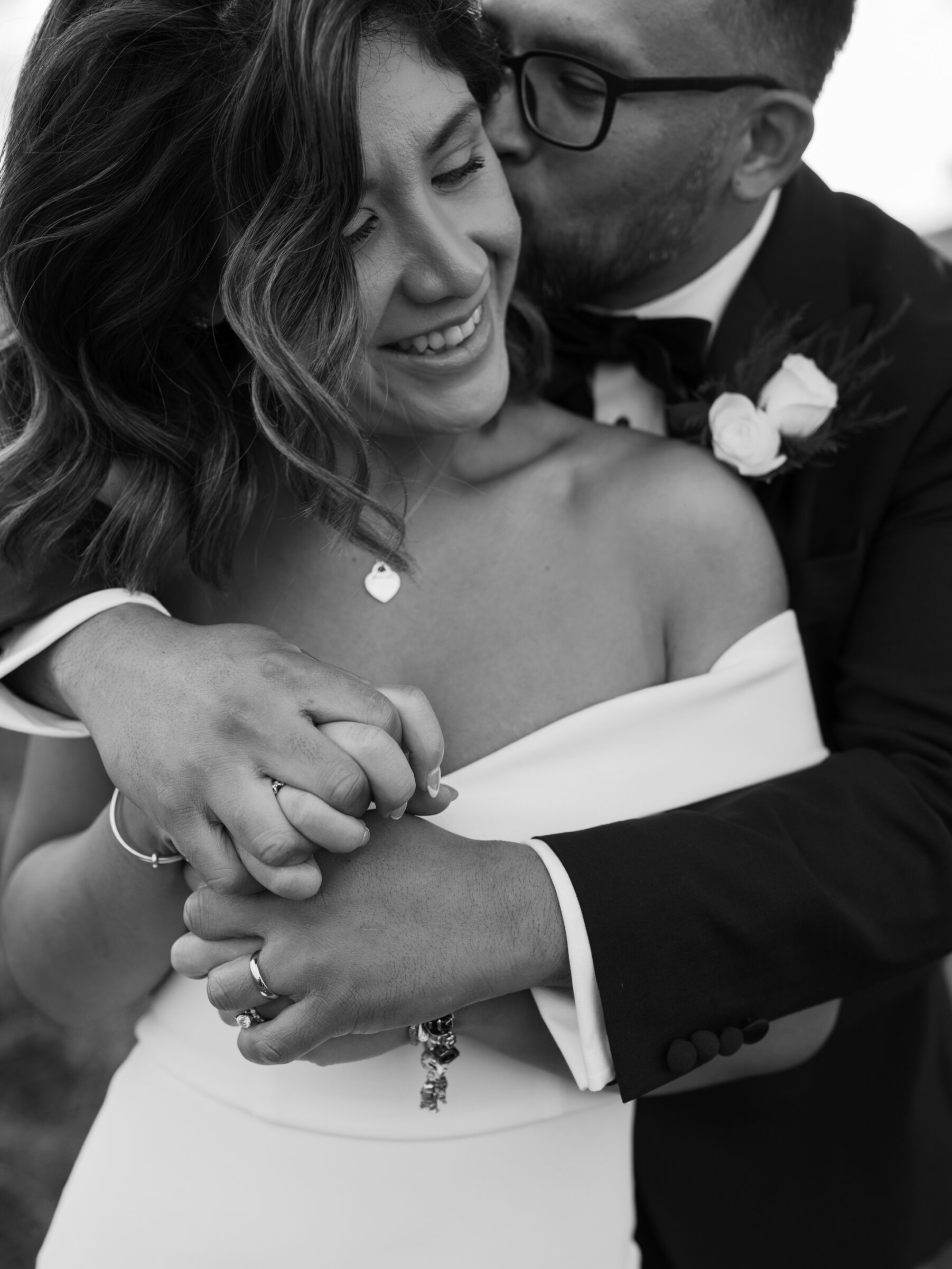 Skyline Drive Virginia Pictures | Black and white close-up of the groom embracing the bride from behind, holding her hands as he kisses her cheek during their mountain meadow portraits.