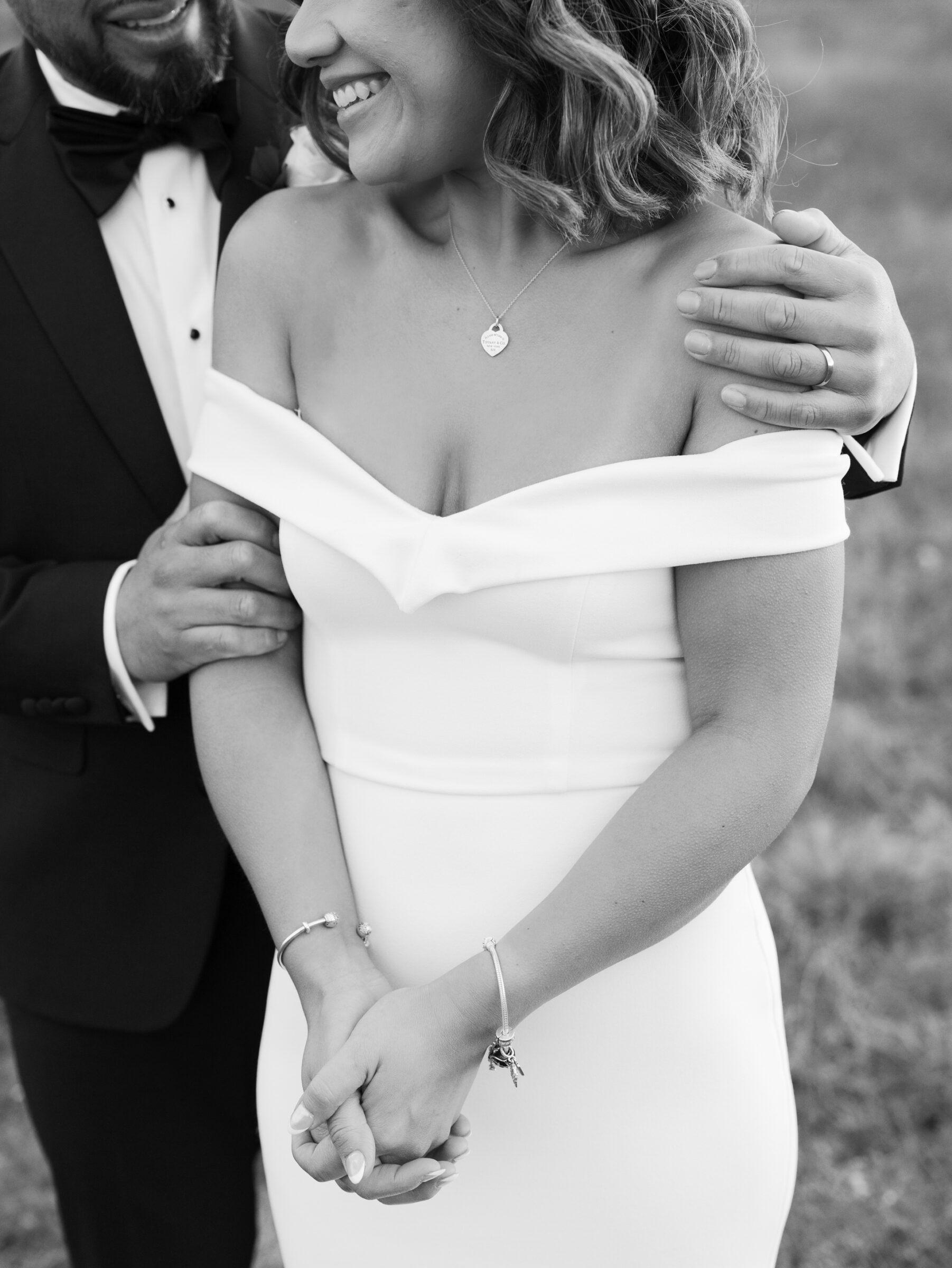 Skyline Drive Virginia Pictures | Black and white close-up of the bride and groom holding hands and smiling as he gently rests his hand on her shoulder during their meadow portraits.